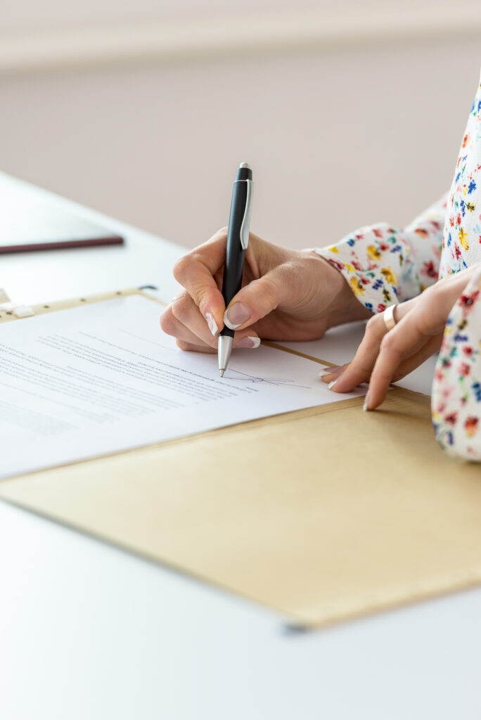 Closeup of businesswoman signing contract in a folder on her office desk.